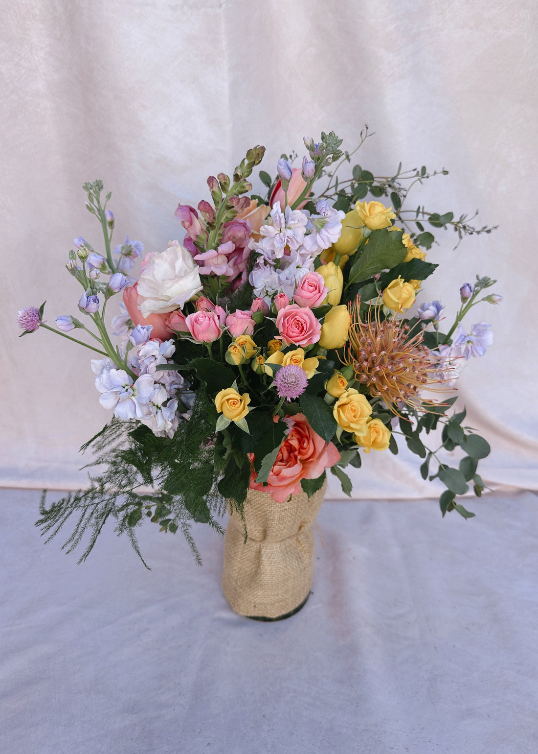 Bouquet of flowers in a burlap vase against a plain background